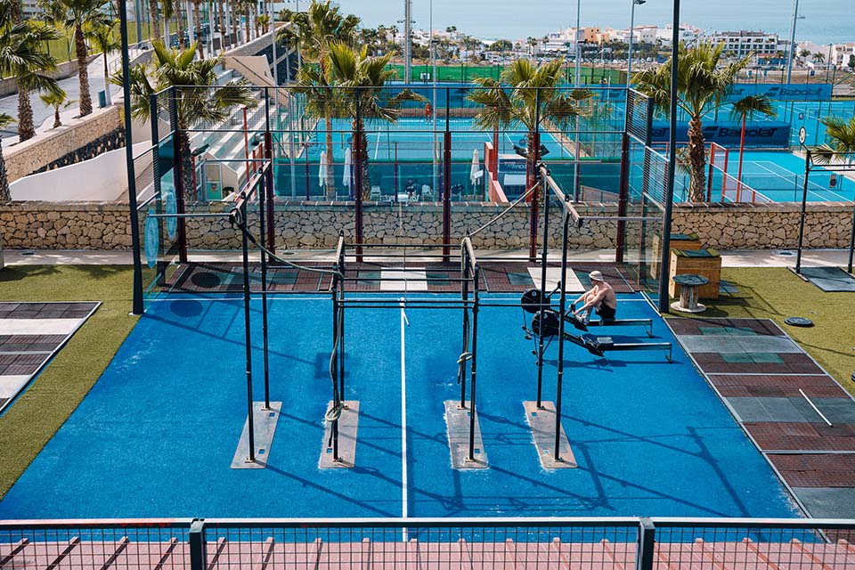 Outdoor calisthenics station with pull-up bars and rings, padel courts behind.