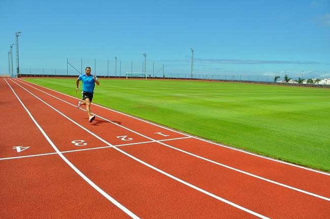 Runner sprinting on an athletics track beside a grass infield.