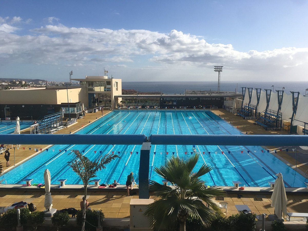 Wide view of outdoor 50 m pool with lane lines and seaside backdrop.