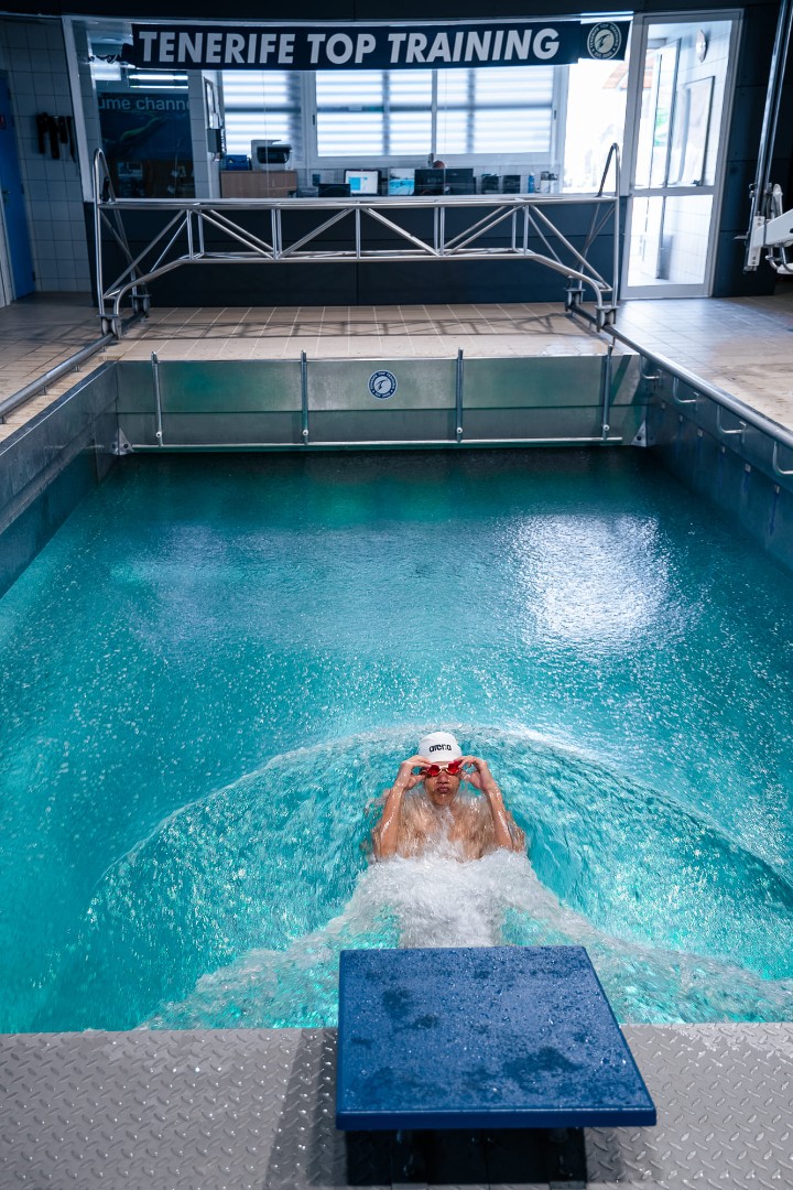 Indoor cold plunge pool used for recovery, with a swimmer at the wall.