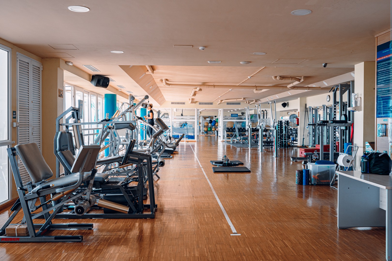 Spacious gym with strength machines and functional training area on wooden flooring.