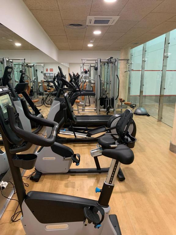 Small gym with stationary bikes and cable machines next to a glass squash court.