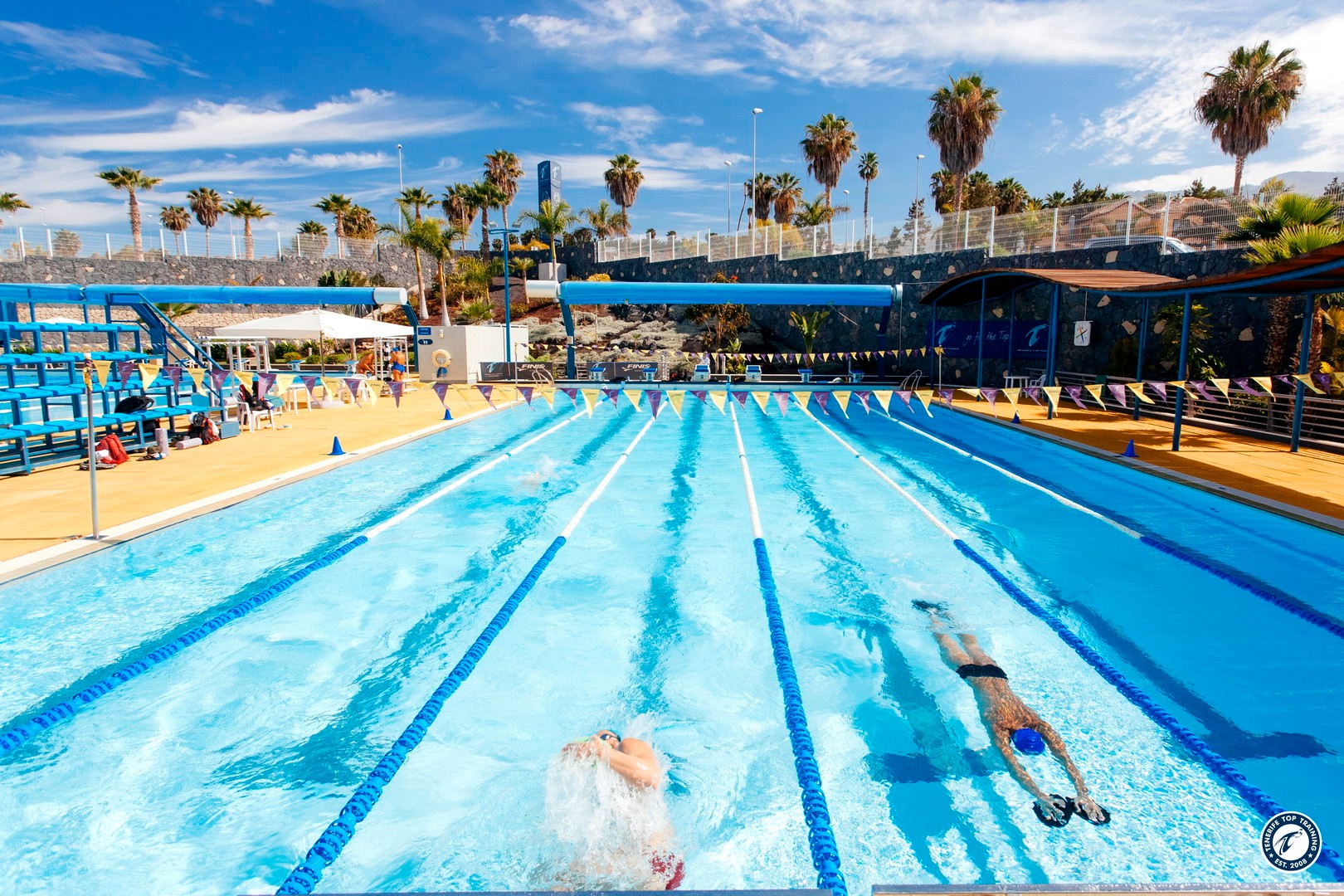 Two swimmers doing laps in an outdoor training pool with lane lines and flags.
