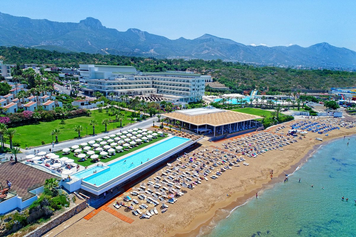 Aerial view of resort with pools, beach umbrellas, and mountains in background