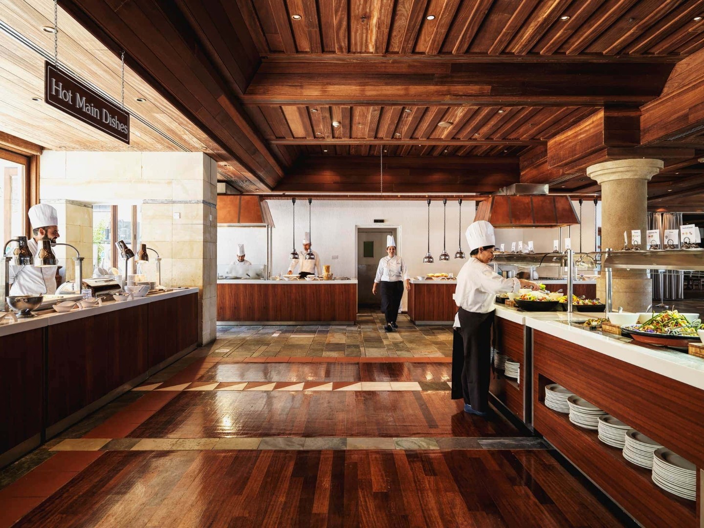 Chefs preparing food in a hotel buffet restaurant with wooden floors and serving stations