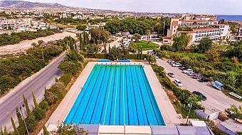 Aerial view of long-lane swimming pool with parking area and landscape in the background