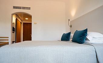Hotel bedroom with large bed, gray bedding, and teal cushions in a minimalist design