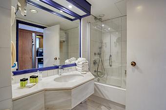 Bathroom with white tiles, bathtub, and counter with toiletries and folded towels