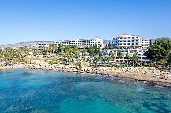 Seaside hotel complex with white buildings and palm trees overlooking a clear blue coastline