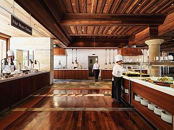 Chefs preparing food in a hotel buffet restaurant with wooden floors and serving stations