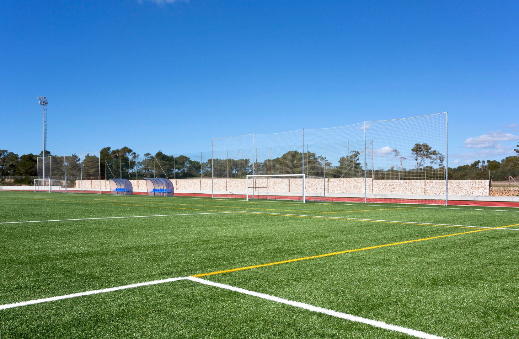 Vue large du terrain de football en gazon synthétique sous un ciel partiellement nuageux.