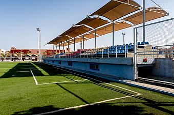 Covered seating area with blue chairs along the edge of a football field