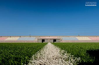 Low-angle view across football pitch showing stadium seating with multicolored stands