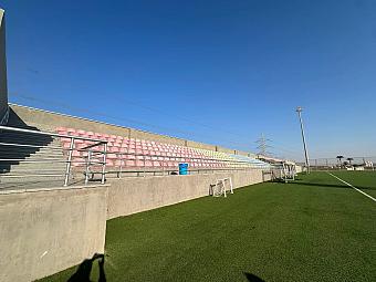 Concrete stands with pastel-colored seats beside the football training camp field