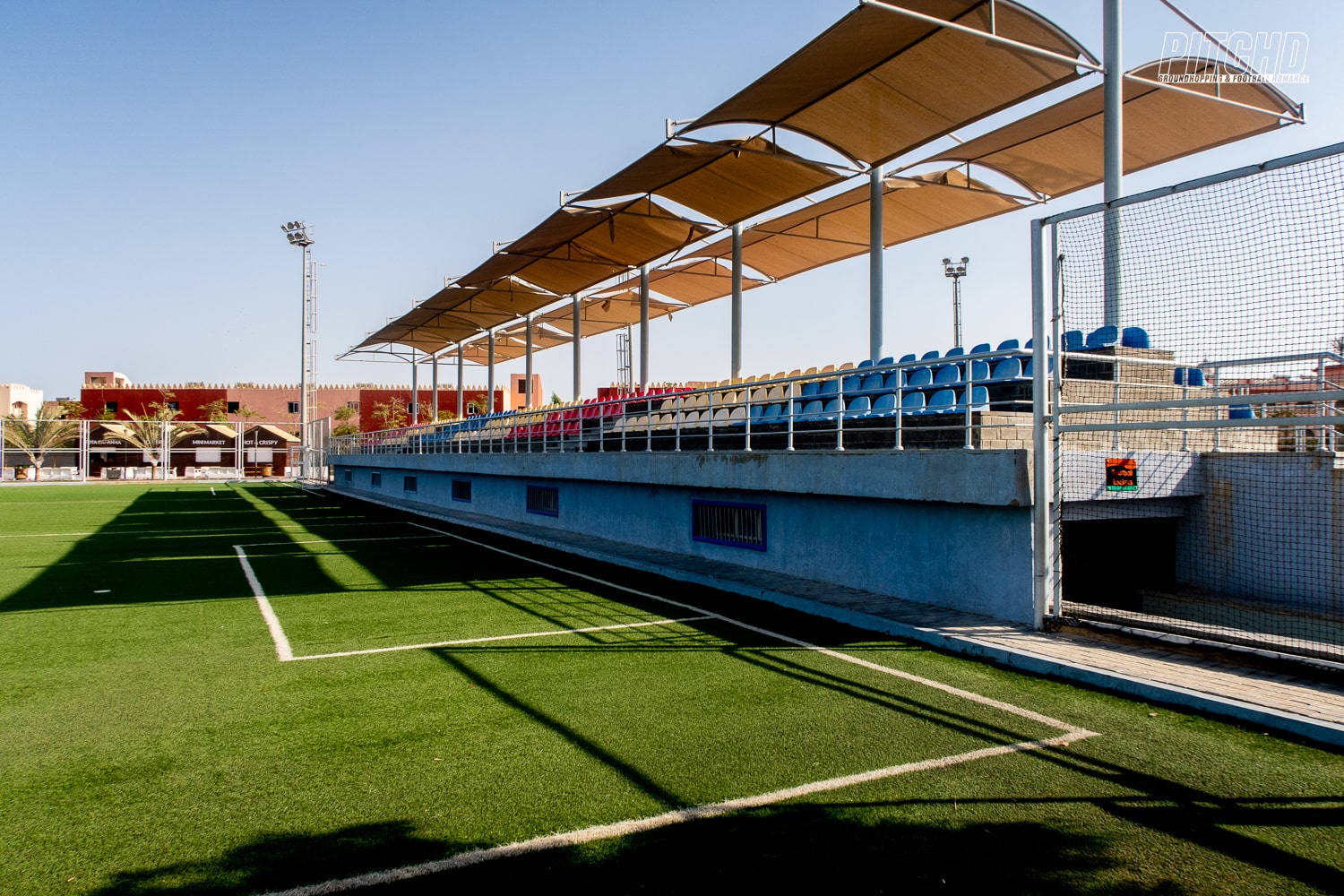 Covered seating area with blue chairs along the edge of a football field