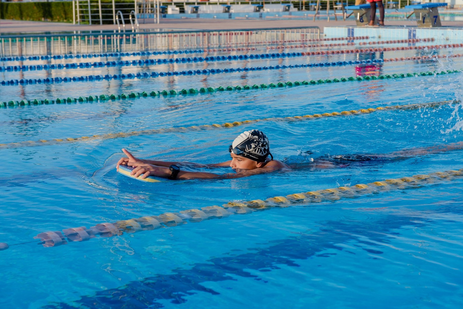 Swimmer in cap training with kickboard in outdoor Olympic-size pool