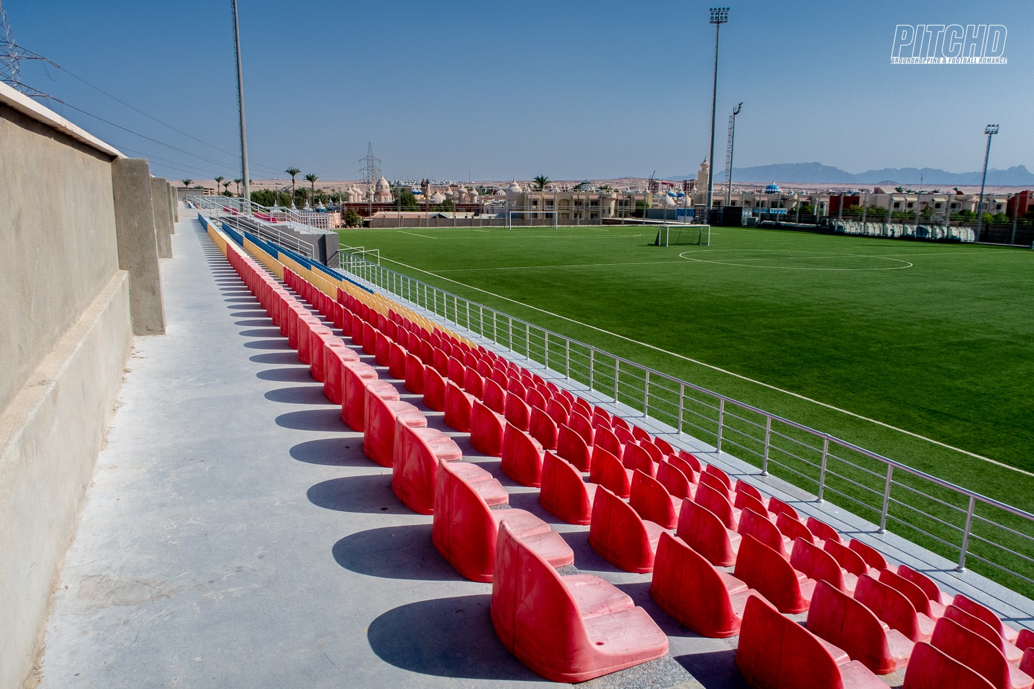 Row of red plastic seats overlooking the football training camp field