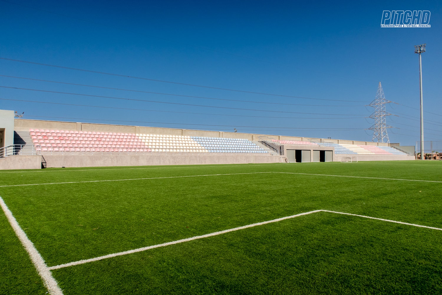 Football field corner view with pastel-colored seating stands under clear sky