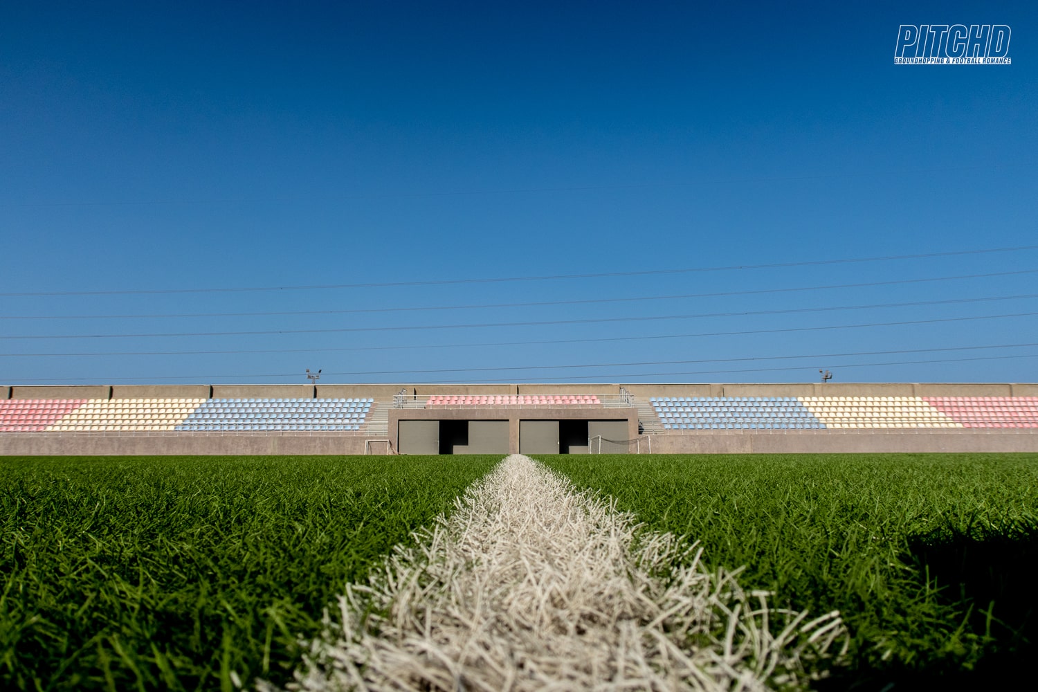 Low-angle view across football pitch showing stadium seating with multicolored stands