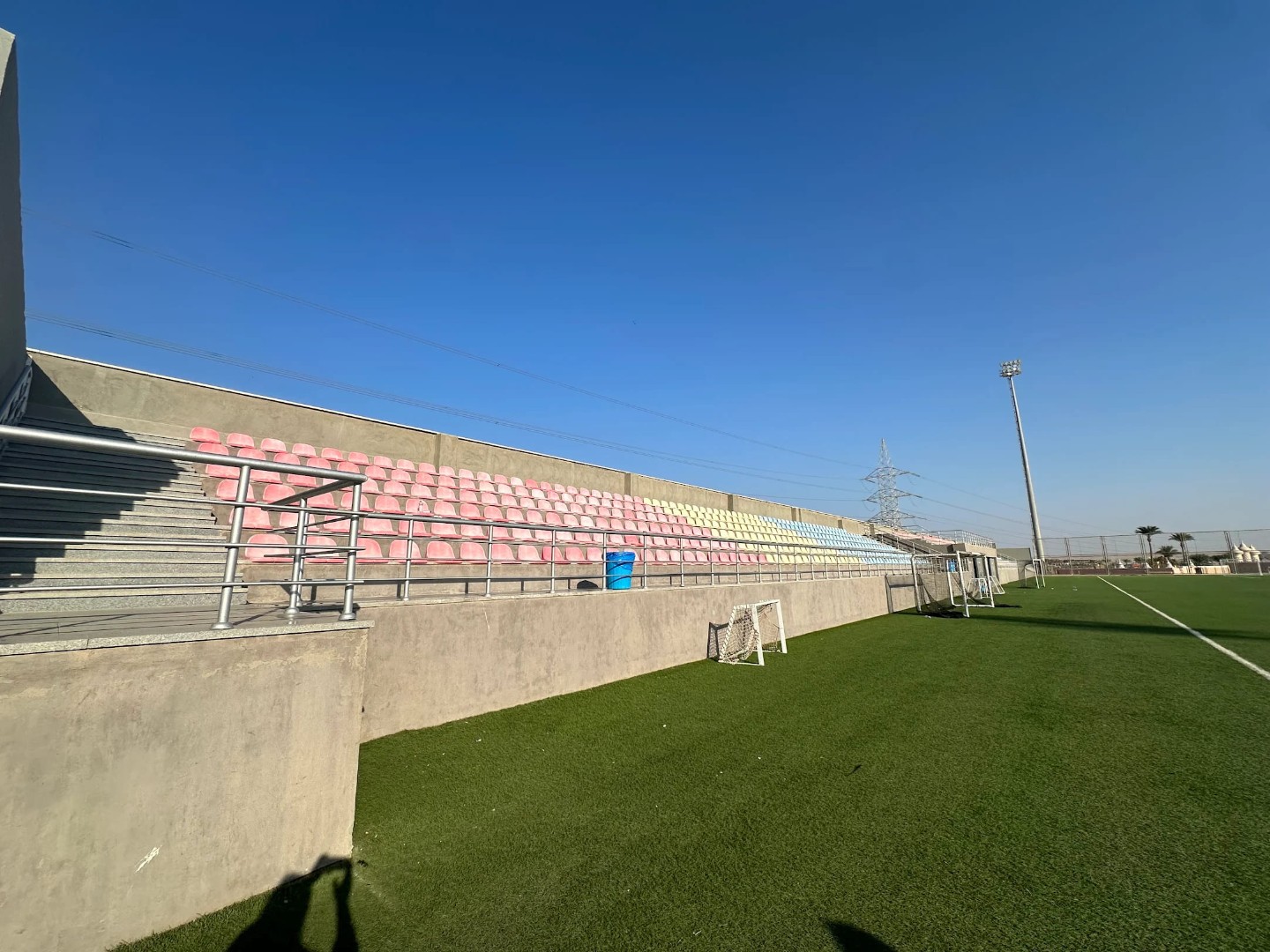 Concrete stands with pastel-colored seats beside the football training camp field