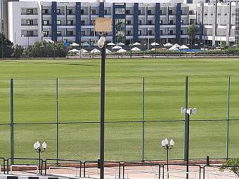 Green football field enclosed by a fence with adjacent resort buildings for training sessions and drills