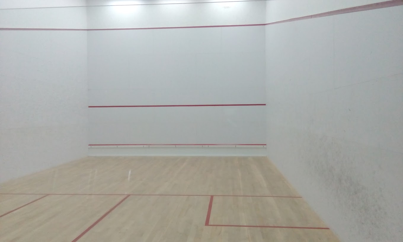 Empty indoor squash court with wooden floor and red boundary lines, ready for training drills.