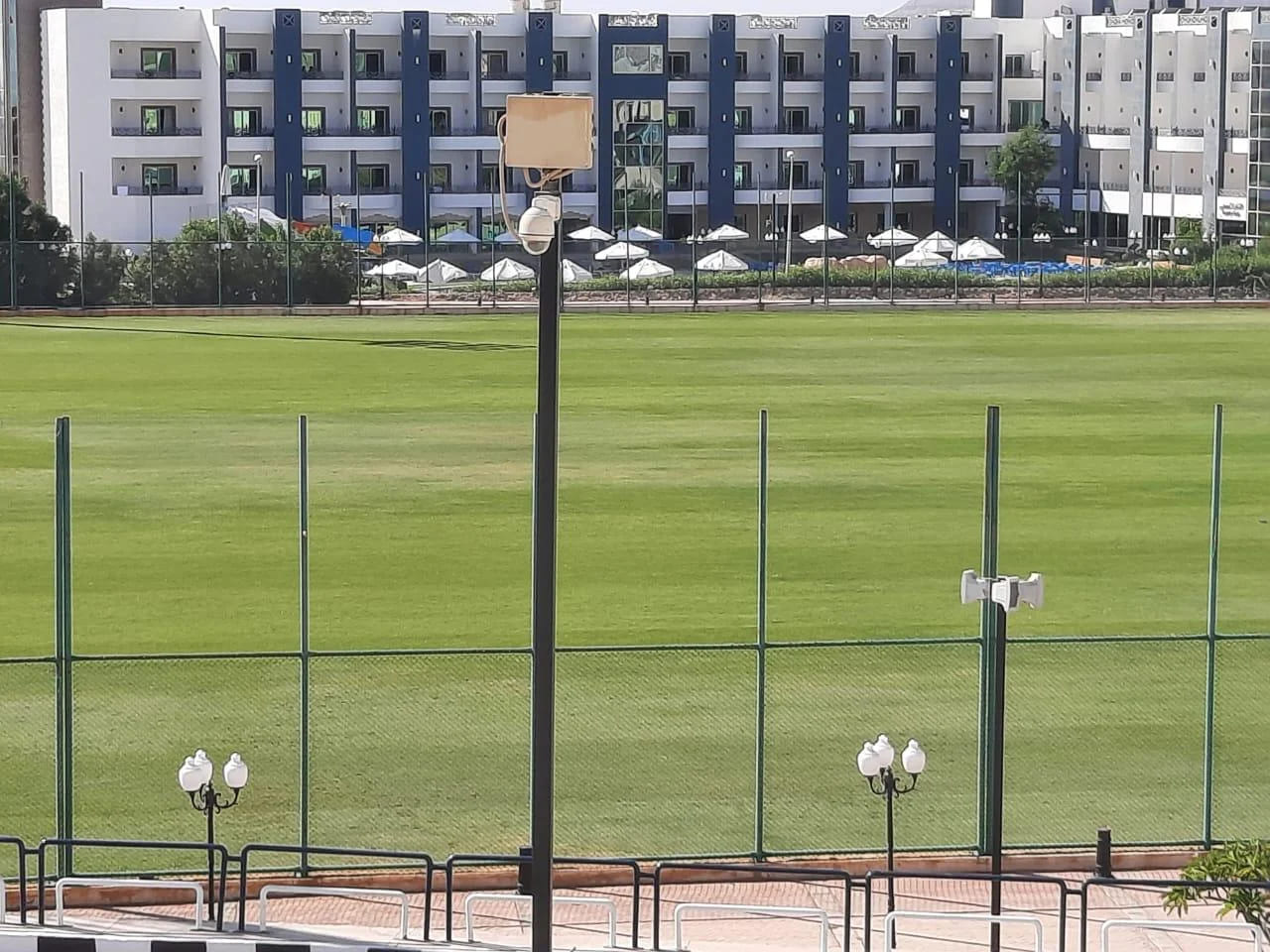 Green football field enclosed by a fence with adjacent resort buildings for training sessions and drills