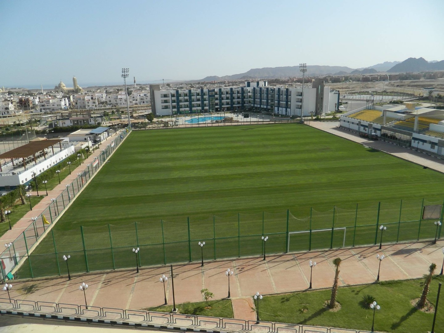 Green football field with goalposts, fenced perimeter, and training areas near sports complex