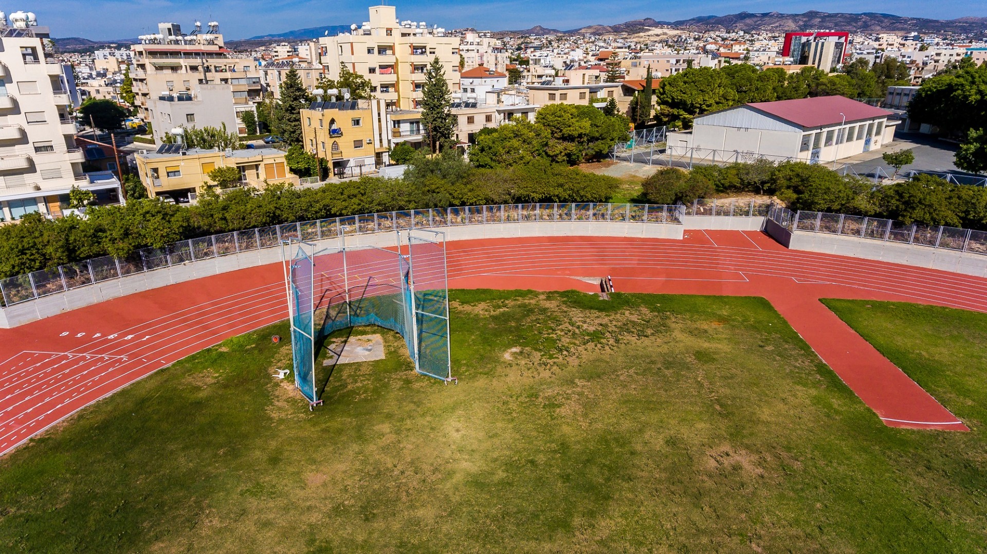 Aerial view of red running track and green field surrounded by city buildings