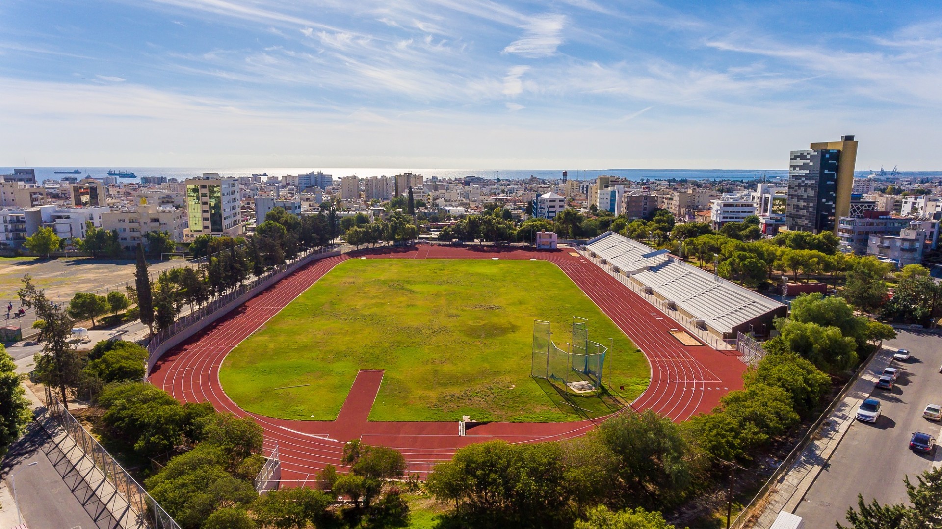Wide view of athletics stadium with track, field, and bleachers near the sea