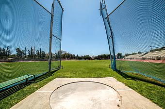 Hammer throw training area with safety nets and grass field under clear blue sky
