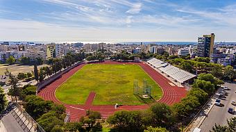 Wide view of athletics stadium with track, field, and bleachers near the sea