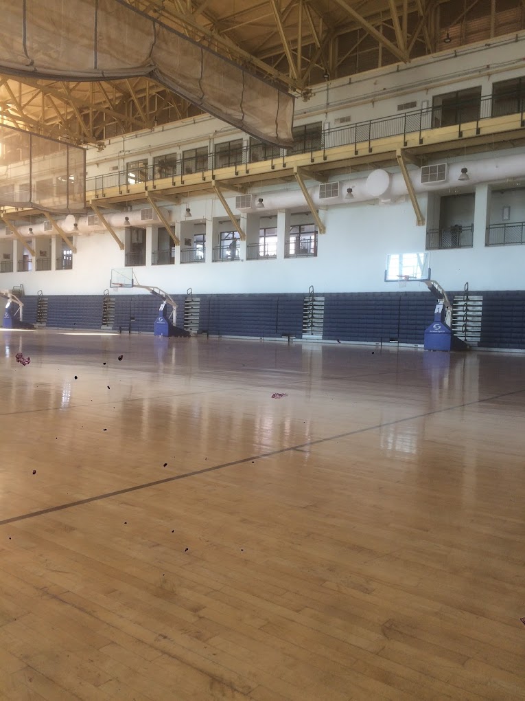 Große Sporthalle mit leerem Holzboden, Basketballkörben und eingeklappten Tribünen.