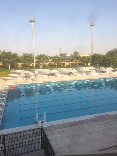 Großes Freibad mit Bahnmarkierungen, umgeben von leeren Tribünen und Flutlichtmasten.
