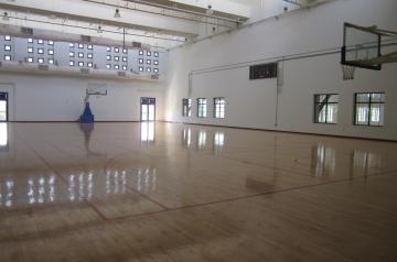 Leere Sporthalle mit poliertem Holzboden und einem Basketballkorb.