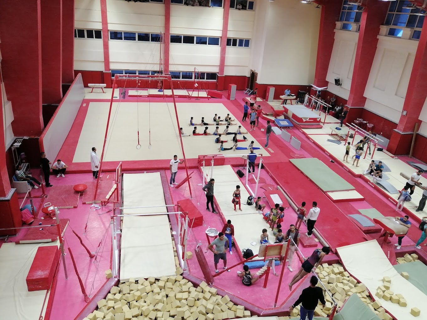 Gymnastics training hall with apparatus, mats, and a foam pit during practice.