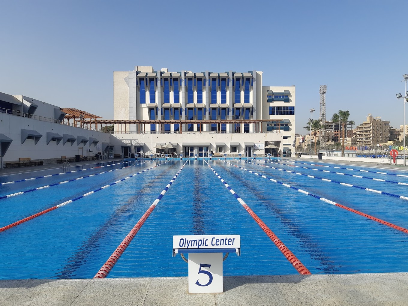 Outdoor Olympic-size swimming pool with lane ropes and a starting block.