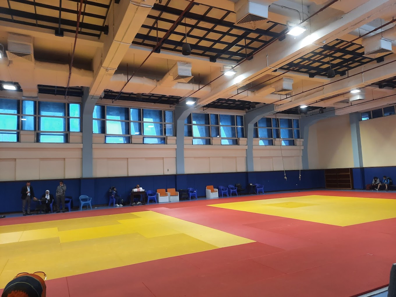 Indoor martial arts hall with large tatami-style mats and seating along the wall.