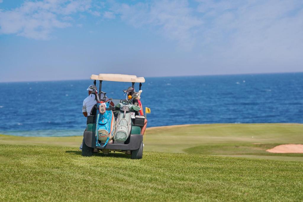 Golf cart with bags on a coastal fairway, ocean backdrop; golfers preparing for a practice round.