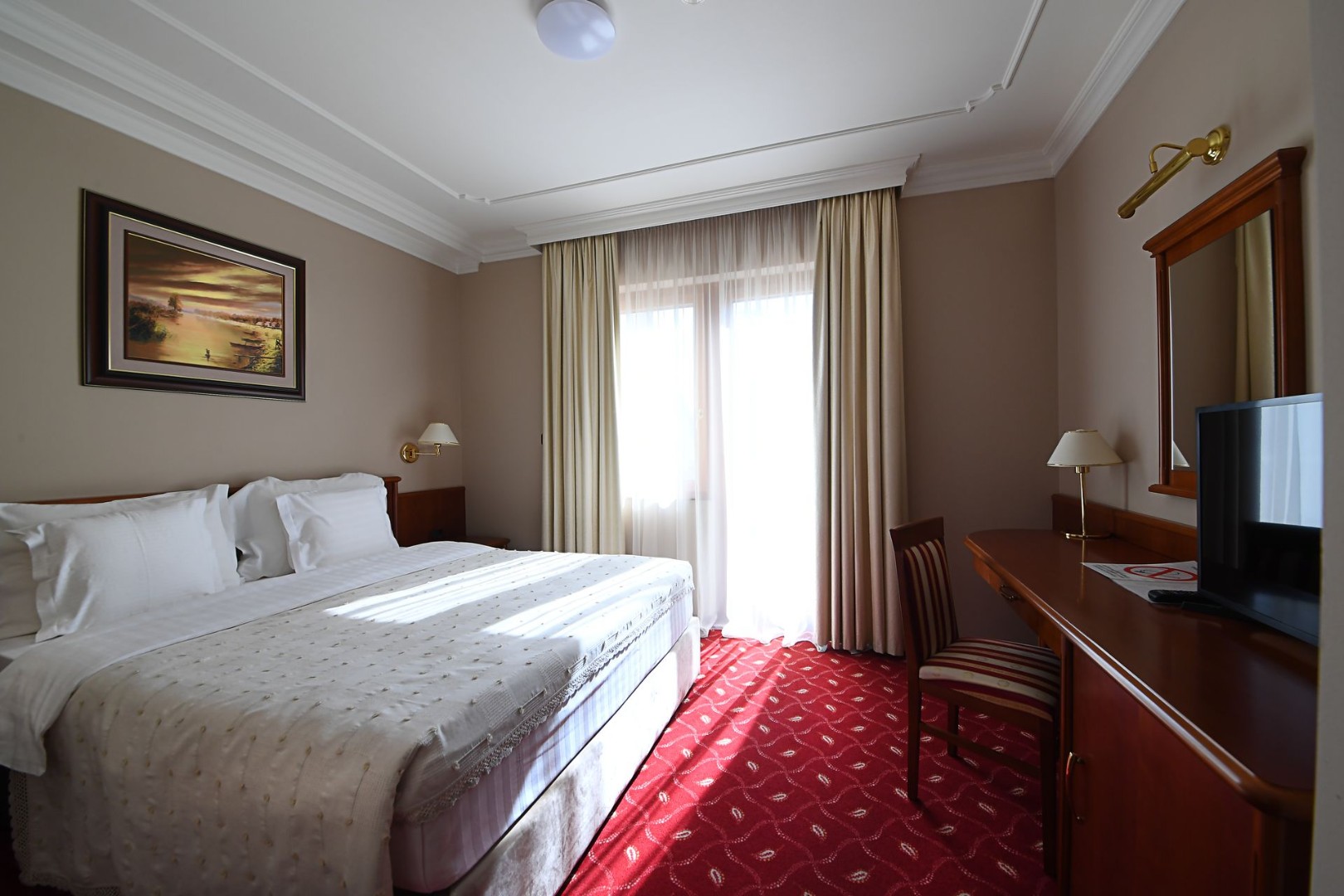 Double room with large bed, desk, TV and window with curtains.