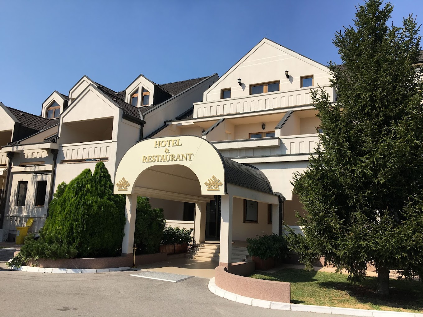 Exterior view of the hotel and restaurant entrance with covered driveway and landscaped greenery.