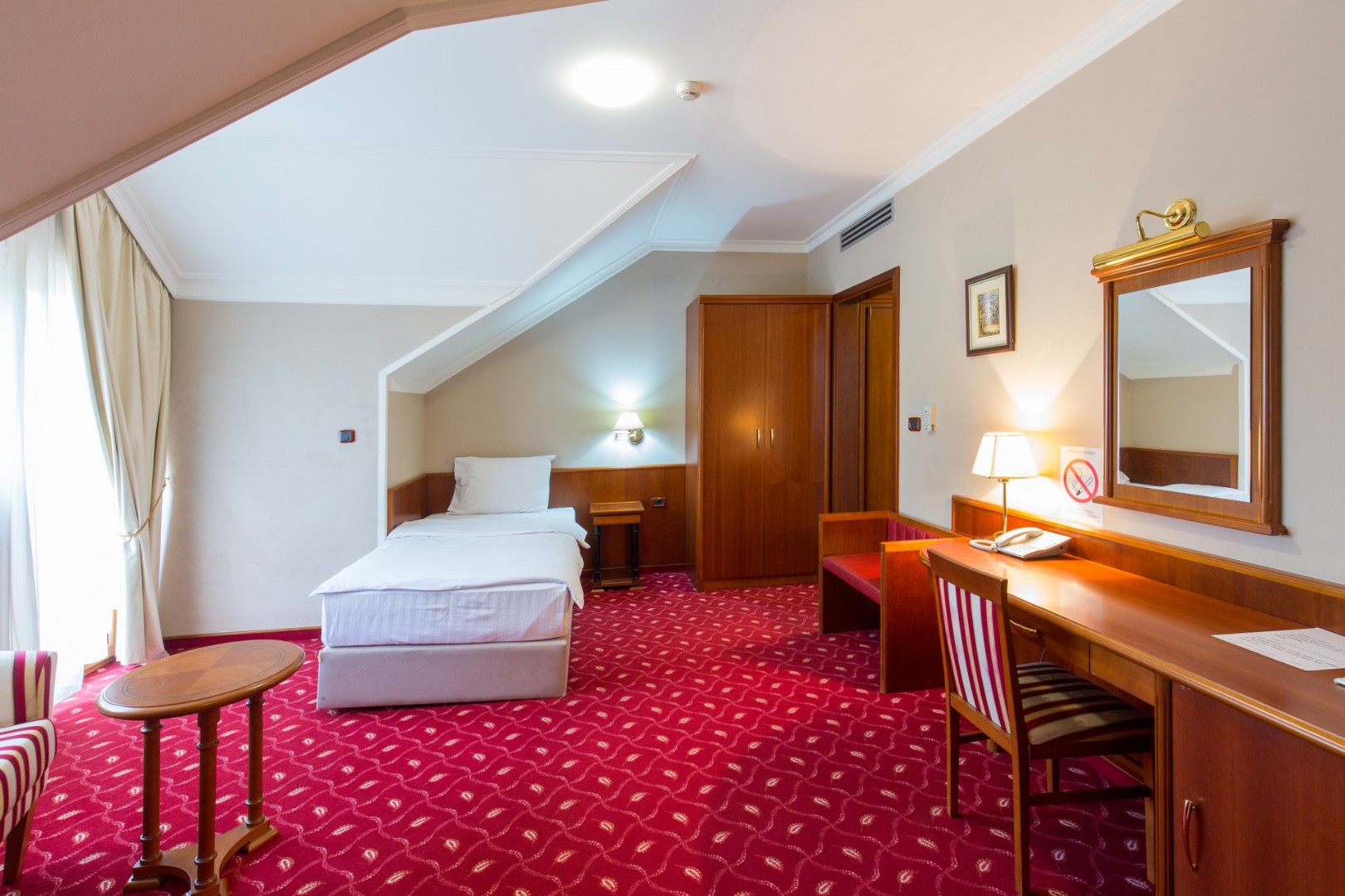 Single room with one bed, desk and wardrobe under a sloped ceiling.