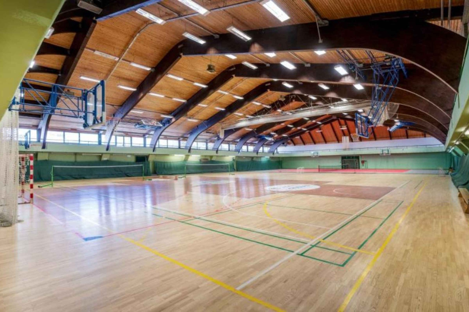 Wide view of indoor multi-sport hall with basketball hoops and court markings.