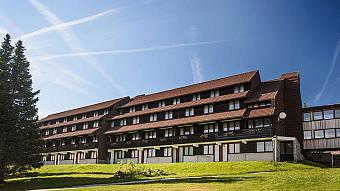 Exterior view of the hotel building with balconies, sloped roof, and surrounding green lawn.