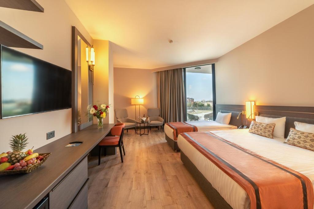 Bright twin room with desk, wall-mounted TV, seating area, and balcony door.