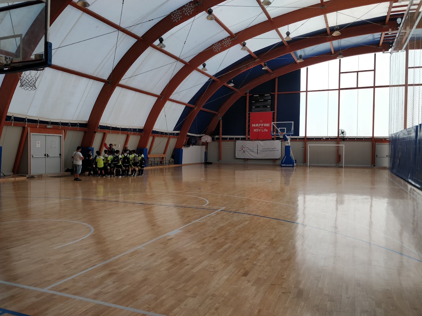 Indoor basketball court; youth athletes and coach huddle near the sideline during a training camp.