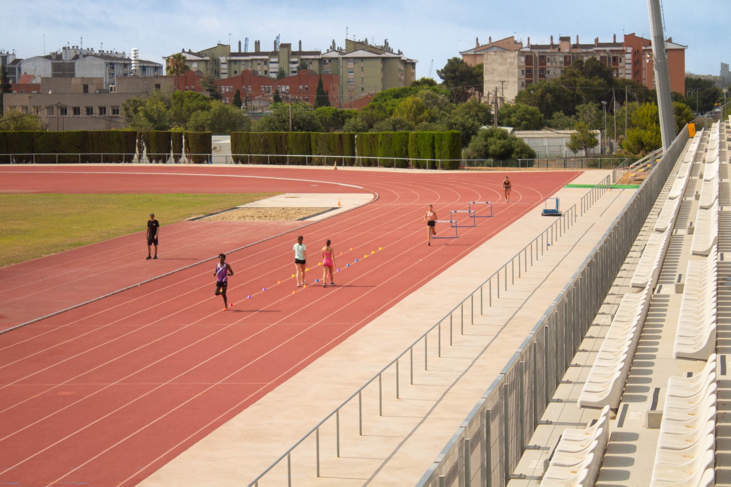 Athleten absolvieren Hürdendrills auf der Bahnkurve neben der Tribüne während des Trainings.