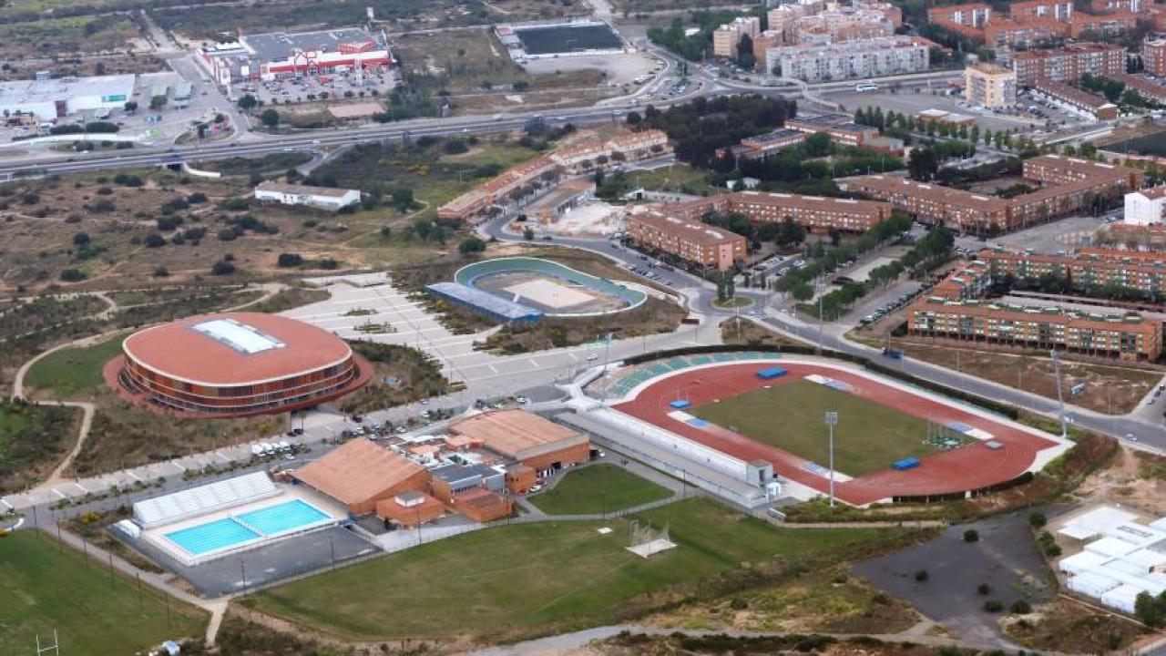Luftaufnahme eines Sportkomplexes mit Leichtathletikstadion, Freibad und nahegelegenen Gebäuden.