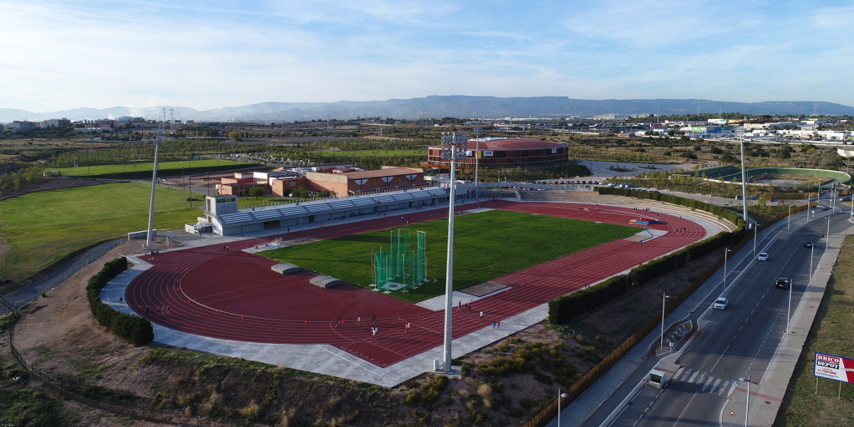 Luftaufnahme eines Leichtathletikstadions mit roter Bahn, Innenfeld, Wurfkäfig und Flutlichtmasten.