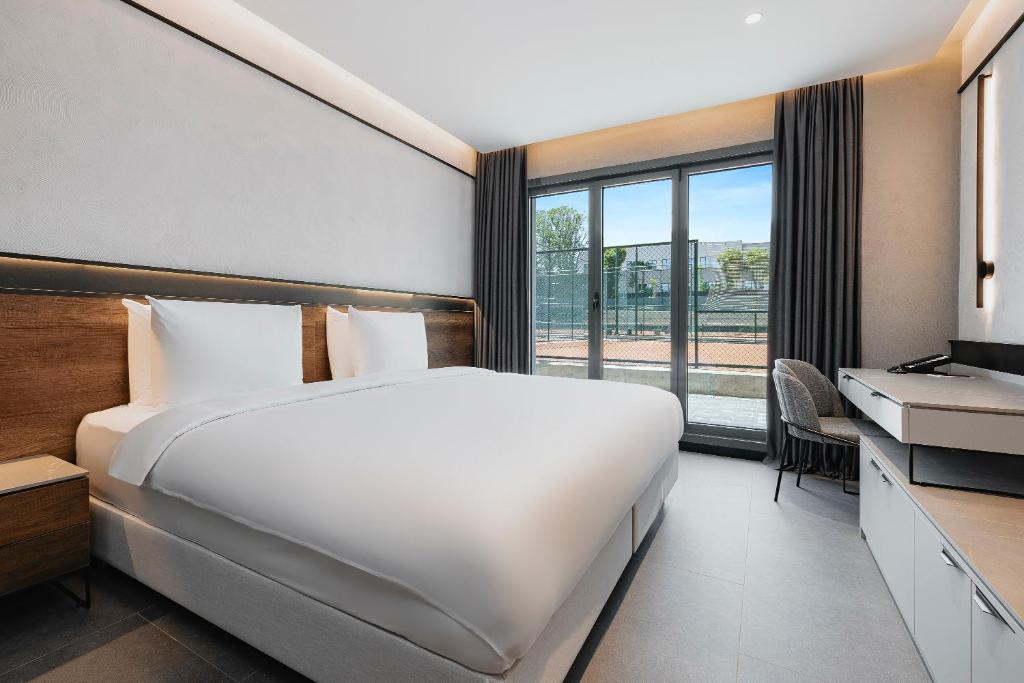 Modernes Doppelzimmer mit Kingsize-Bett, Arbeitsbereich und Balkontüren mit Blick auf die Tennisanlage.